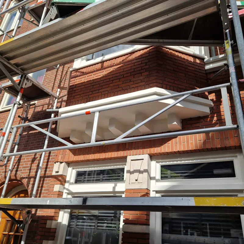 Wit geschilderde gevelonderdelen en kozijnen aan een bakstenen pand in Amsterdam